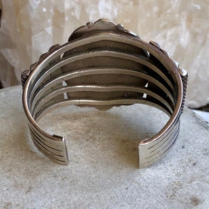 Puede incluir: Un brazalete de plata con un dise&ntilde;o decorativo en la parte delantera. El brazalete est&aacute; hecho de m&uacute;ltiples bandas de plata y tiene una marca estampada en la parte posterior.