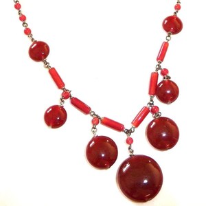May include: A red glass bead necklace with a silver chain and large red glass beads. The necklace has a dangling design with several large red beads.