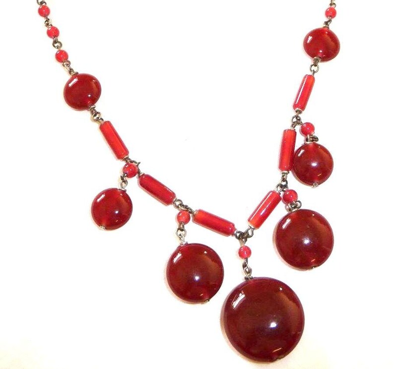 May include: A red glass bead necklace with a silver chain and large red glass beads. The necklace has a dangling design with several large red beads.