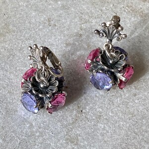 May include: A pair of silver earrings with a floral design and purple and pink gemstones.