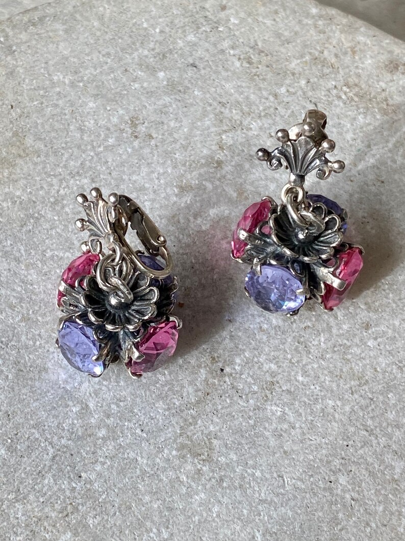 May include: A pair of silver earrings with a floral design and purple and pink gemstones.