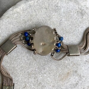 May include: A silver bracelet with a round, ornate charm and blue beads. The charm has the number "900" stamped on it.