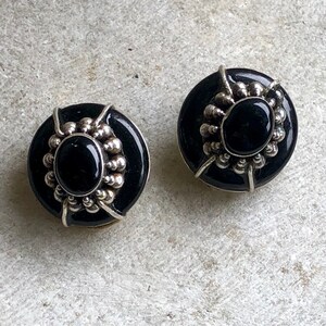 May include: A pair of black onyx earrings with silver settings. The earrings are round and have a beaded design around the onyx stones.