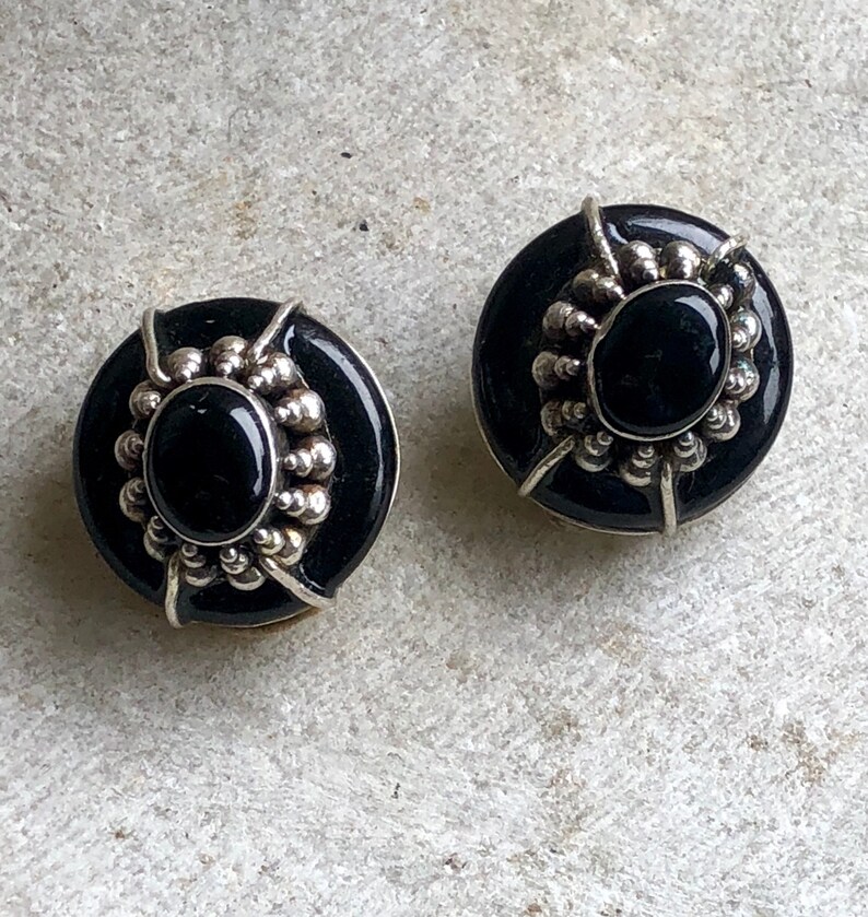 May include: A pair of black onyx earrings with silver settings. The earrings are round and have a beaded design around the onyx stones.