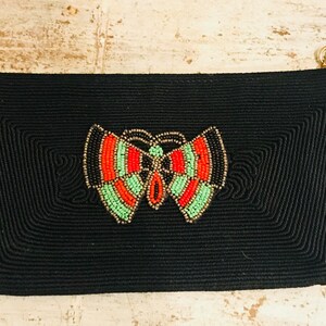 May include: Black beaded clutch with a colorful butterfly design. The butterfly is made of beads in shades of red, green, and black.