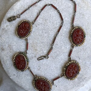 May include: An antique necklace featuring oval, reddish-brown cameos with floral carvings. The cameos are set in a silver-toned metal with a beaded border and connected by a chain with reddish-brown and silver links. The necklace has a clasp closure.
