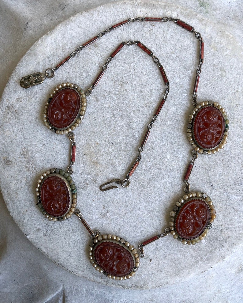 May include: An antique necklace featuring oval, reddish-brown cameos with floral carvings. The cameos are set in a silver-toned metal with a beaded border and connected by a chain with reddish-brown and silver links. The necklace has a clasp closure.