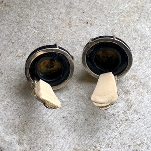 May include: A pair of black and silver clip-on earrings with a round, black stone center.