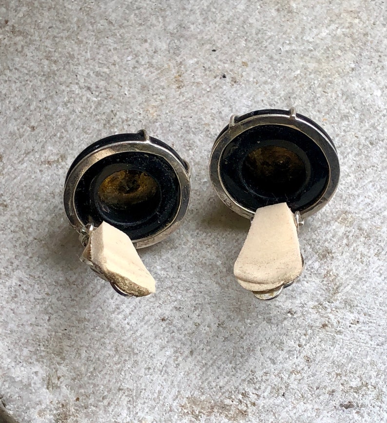 May include: A pair of black and silver clip-on earrings with a round, black stone center.