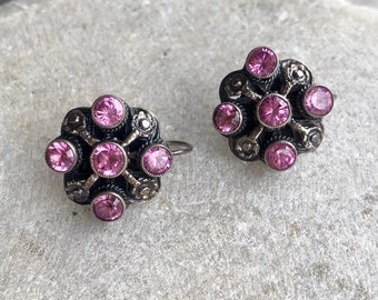 May include: A pair of silver earrings with a floral design and pink gemstones.