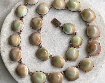 May include: A vintage necklace with a gold chain and 18 iridescent green and brown oval-shaped stones.