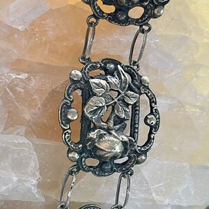 May include: A silver chain necklace with three ornate pendants featuring floral designs. Each pendant has a delicate, intricate design with leaves and a flower.