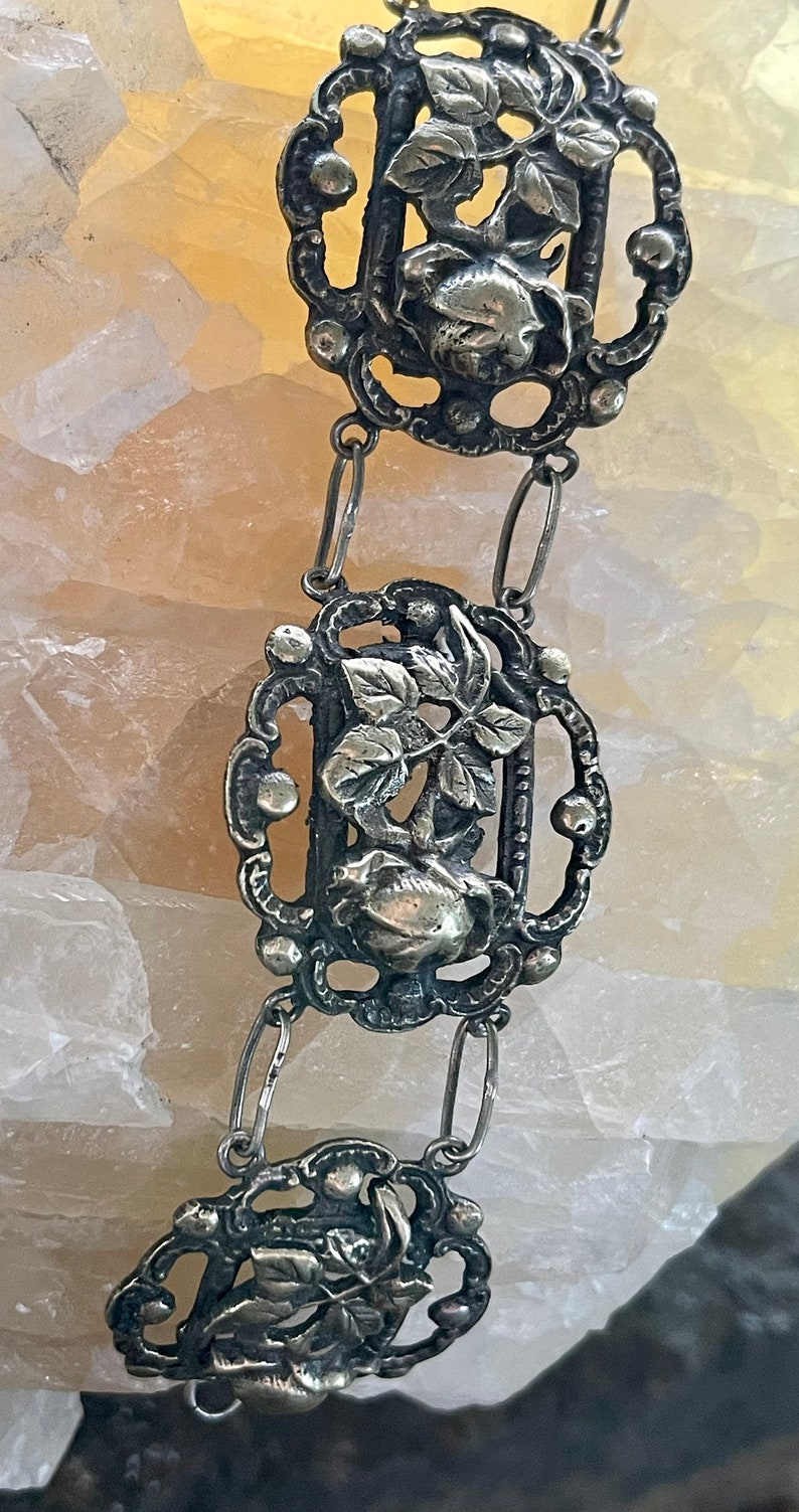 May include: A silver chain necklace with three ornate pendants featuring floral designs. Each pendant has a delicate, intricate design with leaves and a flower.