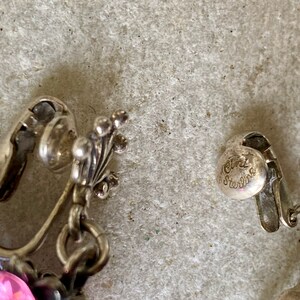 May include: Close-up of a pair of silver clip-on earrings with pink and purple stones. The earrings are marked "925 Sterling".
