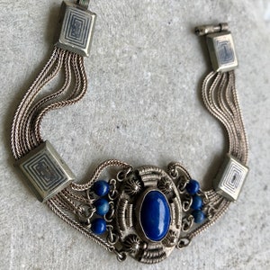 May include: A silver bracelet with a blue lapis lazuli stone and smaller blue beads. The bracelet has a chain-like design and square-shaped clasps.