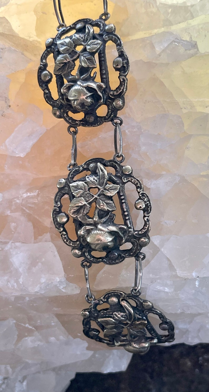 May include: A silver chain necklace with three decorative pendants featuring floral designs. Each pendant is intricately detailed with a rose and leaves.