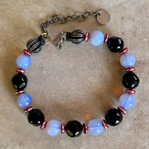 May include: A bracelet with black, blue, and pink beads. The bracelet has a silver clasp with the word "remarkable" on it.
