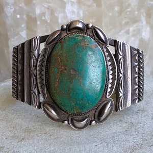 Puede incluir: Un brazalete de plata con una gran piedra ovalada de turquesa engastada en el centro. El brazalete est&aacute; decorado con intrincados dise&ntilde;os de plata.