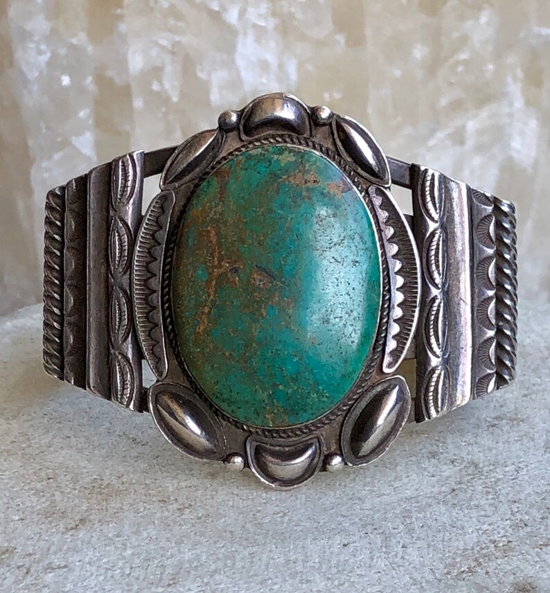 Puede incluir: Un brazalete de plata con una gran piedra ovalada de turquesa engastada en el centro. El brazalete est&aacute; decorado con intrincados dise&ntilde;os de plata.