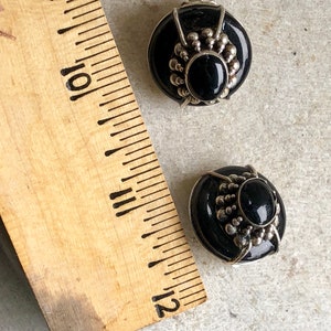 May include: A pair of black and silver clip-on earrings with a round, black stone in the center. The earrings have a silver design around the stone.