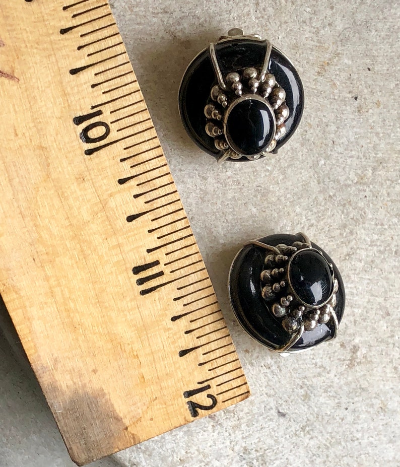 May include: A pair of black and silver clip-on earrings with a round, black stone in the center. The earrings have a silver design around the stone.