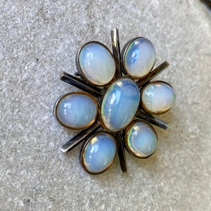 K&ouml;nnte beinhalten: Eine silberne Brosche mit einem Sternburst-Design mit sieben schillernden wei&szlig;en Opal-Steinen.