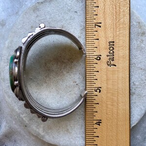 Puede incluir: Un brazalete de plata con una piedra turquesa verde y un dise&ntilde;o decorativo. El brazalete tiene un di&aacute;metro de 5 pulgadas.