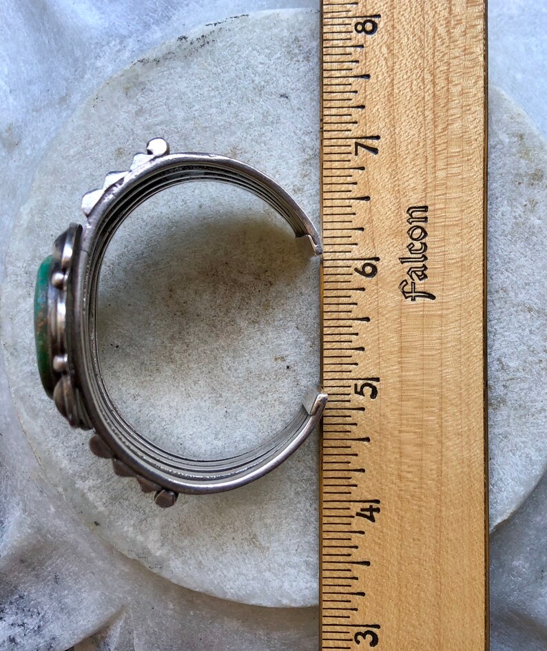 Puede incluir: Un brazalete de plata con una piedra turquesa verde y un dise&ntilde;o decorativo. El brazalete tiene un di&aacute;metro de 5 pulgadas.