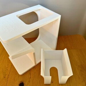 May include: White plastic organizer with two compartments. The larger compartment has a rectangular opening on the top and the smaller compartment has a curved opening on the side.
