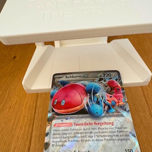 May include: A Pokemon trading card featuring Schlurmx, a red and blue Pokemon with a large, round body and two small arms. The card has a white background with black text and a blue border. The card's ability is "Faustdicke Vergeltung" and its attack power is 150.
