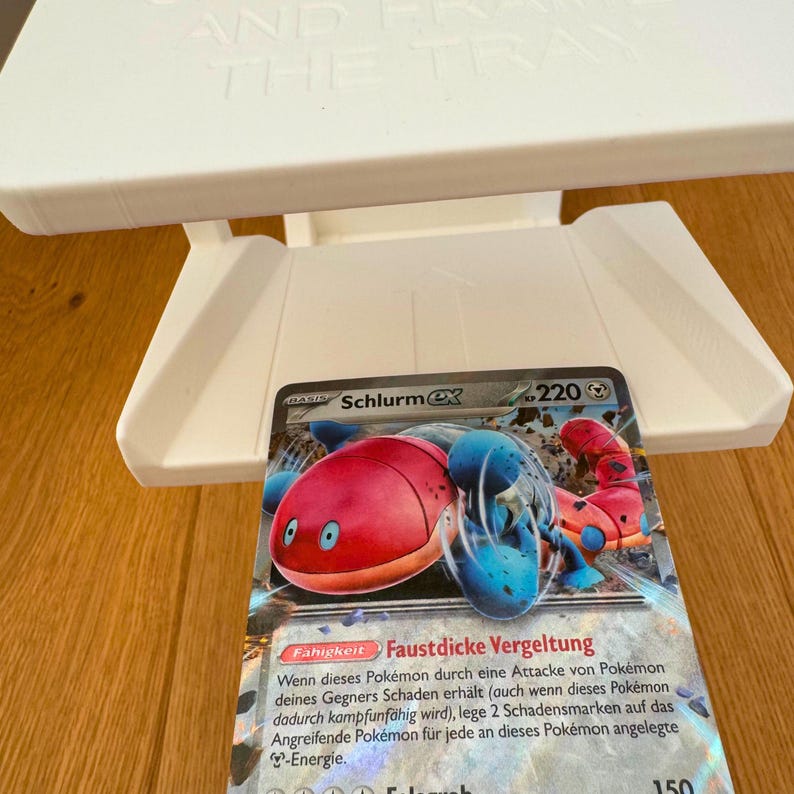 May include: A Pokemon trading card featuring Schlurmx, a red and blue Pokemon with a large, round body and two small arms. The card has a white background with black text and a blue border. The card's ability is "Faustdicke Vergeltung" and its attack power is 150.