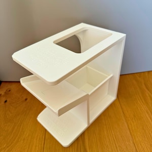 May include: White plastic organizer with three compartments and a top shelf. The top shelf has a cutout for a phone or other device. The organizer is labeled "Organize Your Life" on the top shelf.