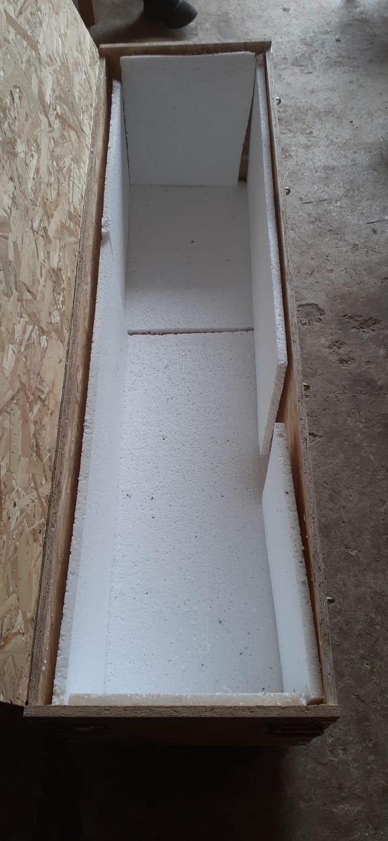 Pu&ograve; includere: Una cassa di legno aperta, rivestita con imbottitura in schiuma bianca. La cassa &egrave; rettangolare, con un esterno marrone chiaro e un interno bianco. L'imbottitura in schiuma serve a proteggere il contenuto durante la spedizione.