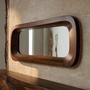 Könnte beinhalten: Ein rechteckiger Holzspiegel mit einem abgerundeten, geschwungenen Rahmen. Der Spiegel hängt an einer Wand mit einer hellbraunen Textur.