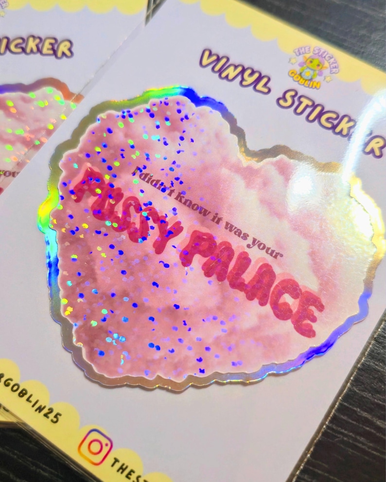 May include: A holographic vinyl sticker with a pink, cloud-like design and the text "FUSSY PALACE" in red. The sticker also includes the phrase "I didn't know it was your" in a smaller font. The sticker has a glittery effect and a scalloped edge.