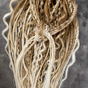 Thin double-sided synthetic dreadlocks with extensions, in beige and blond tones.