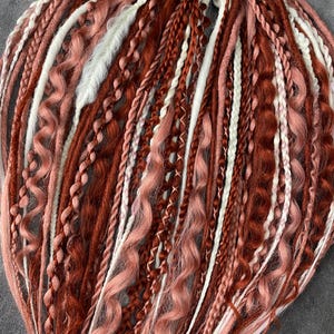 Synthetic dreadlocks in red and powdery colors with the addition of white. DE braids idreads.