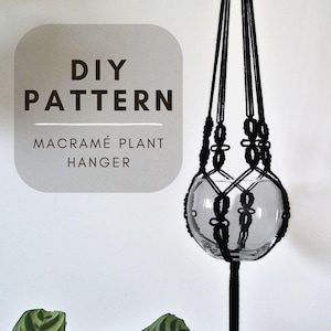 May include: A black macramé plant hanger with a clear glass globe. The hanger is suspended from a black cord and features intricate knotting. The text "DIY PATTERN MACRAMÉ PLANT HANGER" is displayed on a gray background.