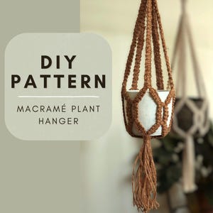 May include: DIY macrame plant hanger pattern. A close-up of a brown macrame plant hanger with a white planter. The hanger is made with a thick, natural fiber rope.