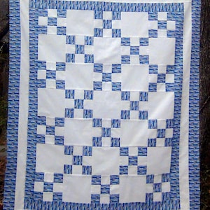 May include: A white quilt with a blue and white patterned border. The quilt is made up of a series of squares, some of which are white and some of which are blue and white.