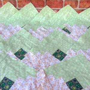 May include: A green and white patchwork quilt with a chevron pattern. The quilt is made of squares of fabric sewn together to create a geometric design.