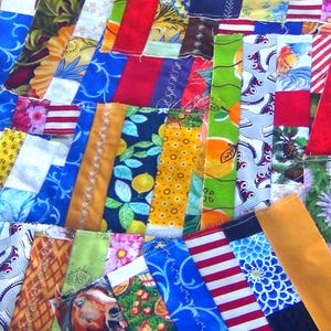 May include: A colorful patchwork quilt with a variety of fabric patterns. The quilt features strips of fabric in various colors, including blue, red, yellow, and green. Some strips have floral patterns, while others have stripes or solid colors. The quilt is handmade.