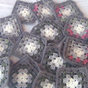 May include: A collection of crocheted granny squares in shades of gray, white, and green with a few pink accents. The squares are arranged in a semi-circle pattern.