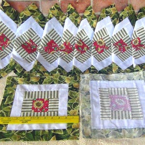 May include: A collection of handmade quilted items featuring a sunflower and floral pattern. The pieces include square placemats and diamond-shaped elements with red and green accents. The overall design has a rustic, country aesthetic.