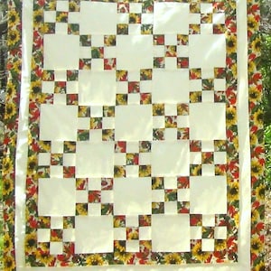May include: A handmade quilt with a cream-colored center featuring a grid pattern of large cream squares and smaller squares with a floral design. The border is a sunflower and leaf pattern.