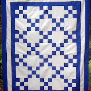 May include: A white and blue quilt with a checkerboard pattern. The quilt is made of squares of white fabric with blue squares sewn into the center of each white square. The quilt is bordered with a blue fabric.