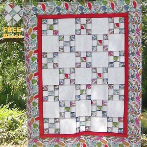 May include: A white quilt with a red border and a colorful floral pattern on the border. The quilt is made up of squares and is a patchwork design.