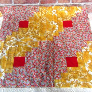 May include: A patchwork quilt with a floral pattern in yellow and white, interspersed with red squares. The quilt features a mix of floral and berry-like designs, creating a vibrant and textured appearance. The quilt is likely handmade.