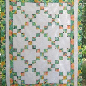 May include: A white quilt with a green and floral border. The quilt is made up of a grid of white squares with smaller green and floral squares in between.