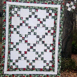 May include: A white quilt with a red and green border featuring a pattern of cardinals and holly. The quilt is made up of squares with a checkerboard pattern.